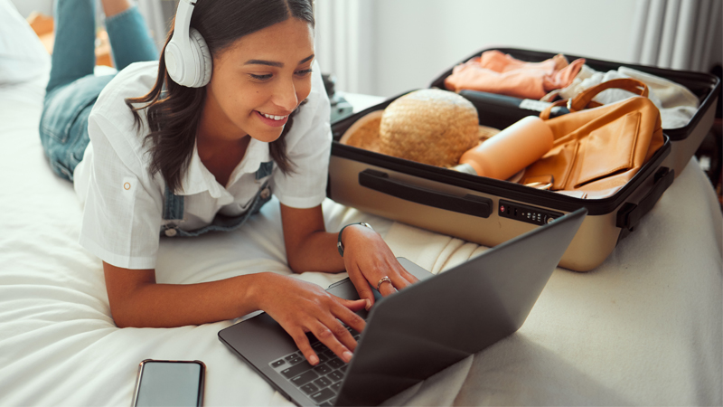 ragazza scrive al pc con a fianco una valigia